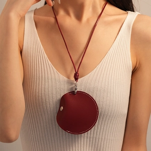 Detail of red circular PU leather necklace pouch with woven lanyard and metal snap button