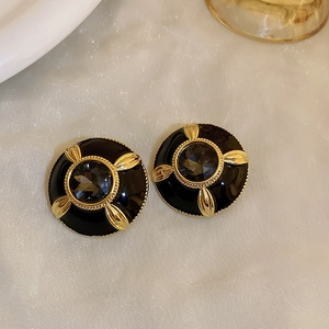 Macro shot of vintage black enamel round earrings with crystal center and gold leaf accents