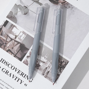 Detail of two gray retractable pens with red wax tips on a minimalist book background