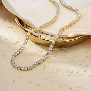 Elegant gold tennis necklace with full cubic zirconia stones on silk champagne background
