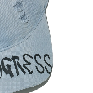 Detail of distressed light blue denim baseball cap with printed lettering on the brim