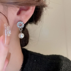 Close-up of a silver diamond-studded round earring with a white pearl drop on model