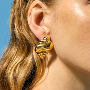 Golden conch-shaped stainless steel earrings on model with blue background