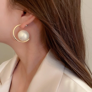Close-up of elegant gold C-shaped earring with white pearl worn by a female model