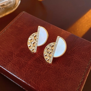 Macro detail of half-moon stud earrings with white mother-of-pearl and gold hollow patterns