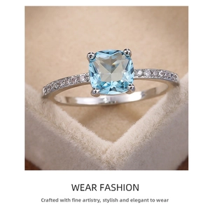 Macro detail of square blue zircon ring with paved side stones in a beige jewelry box