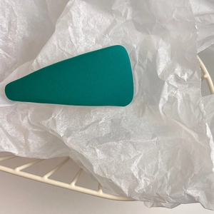 Close-up of a matte dark green triangle hair clip on a textured white background