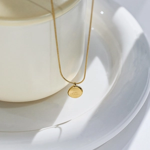 Polished 18k gold plated round pendant necklace with elegant snake chain on white ceramic