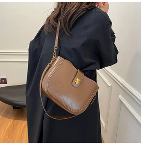 Detail of dark caramel brown leather bucket bag with gold clasp shown on a model