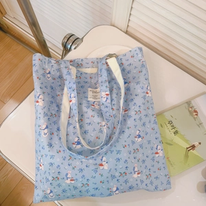 Detail der hellblauen Canvas-Tasche mit weißem Hasen und Blumenmuster auf weißem Stuhl