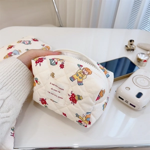 Handheld view of quilted cotton makeup bag with colorful cartoon prints and zipper