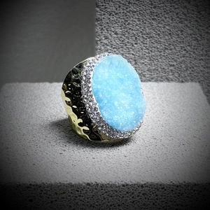 Detail of light blue crystal cluster ring with gold hammered band on grey block