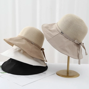Elegant wide brim straw bucket hat with bow accent and metal logo on a gold display stand