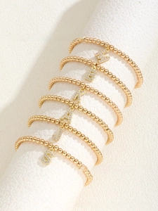 Close-up of golden beaded elastic bracelets featuring rhinestone-studded letter pendants