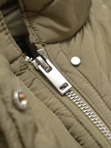 Detailed close-up of high-quality metal zipper and snap buttons on olive green jacket