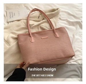 Close-up of pink woven tote bag showing leather strap and brand plaque on bed linen