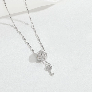 Macro detail of silver necklace featuring heart lock and key pendants with zircon accents