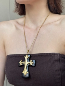 Macro detail of gothic resin cross pendant with golden fleur-de-lis and metallic chain