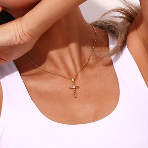Detail shot of a gold-plated stainless steel cross necklace with zircon stone on a model