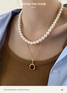 Detail of layered jewelry featuring white pearl strand and golden chain with smoky topaz pendant