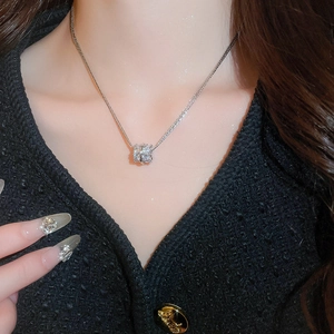 Detail of silver layered zircon cylinder pendant necklace worn on a V-neck sweater