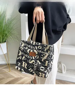 Détail du sac cabas en toile montrant le logo en cuir marron et les anses en nylon