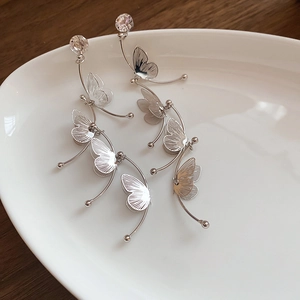 Detail of silver butterfly tassel earrings with sparkling rhinestones on a ceramic dish