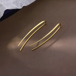Minimalist long golden linear drop earrings on a dark textured background