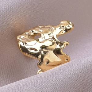Macro shot of irregular molten gold ear cuff with polished finish on champagne silk fabric