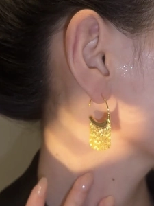 Close-up of golden tassel earrings with sparkling sequin texture worn by a model
