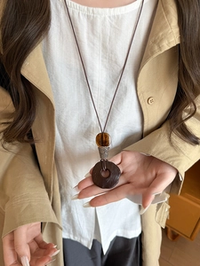 Detail of a large round wood resin pendant with tiger eye bead on a long cord necklace