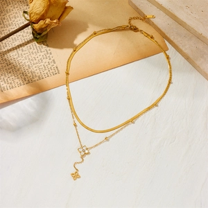 Collier double rang en acier titane doré avec pendentif trèfle sur fond texturé