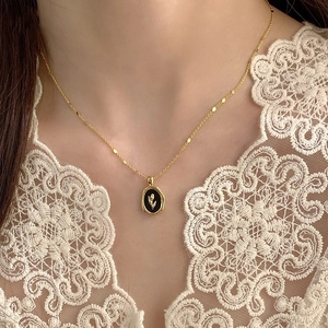 Detail of a gold necklace with a black oval tulip pendant worn with white lace clothing