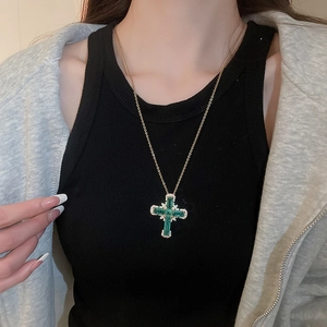 Détail d'un collier pendentif croix doré orné de cristaux verts et de zircons
