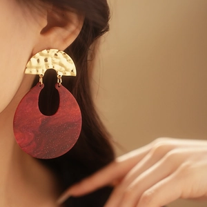 Detail of model wearing vintage red resin hoop earrings with hammered gold metal finish