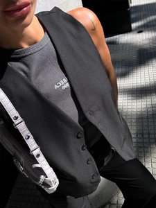 Detail of a black single-breasted vest over a gray ribbed tank top with logo text