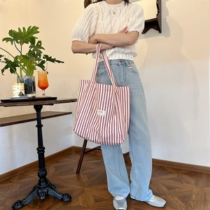 Detail of red and white striped canvas tote bag held by a model in a bright cafe