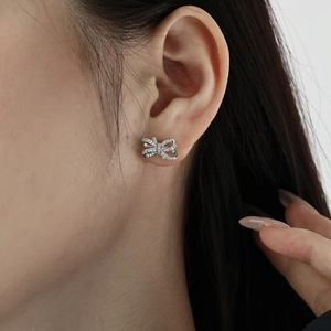 Gros plan de boucles d'oreilles nœud en argent serties de zircons sur l'oreille