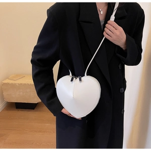 Dettaglio di una borsa a tracolla bianca a forma di cuore indossata su un blazer nero