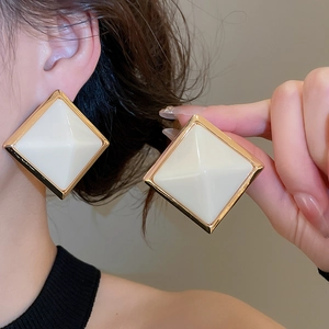 Gros plan de boucles d'oreilles carrées en résine blanc crème et or sur un mannequin