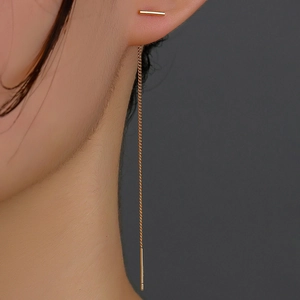 Close-up of golden tassel earring with a linear bar and long chain on model