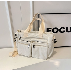 White corduroy tote bag showing front zipper pockets and beige shoulder straps