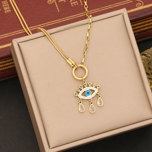 Gold evil eye necklace with blue crystals and tassels on a beige jewelry display box