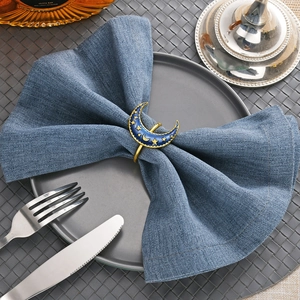 Detail of moon and star enamel napkin ring in navy and gold on a blue linen napkin