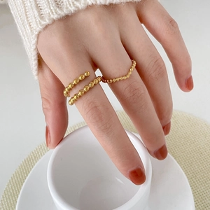 Detail showing gold beaded rings worn on hands holding a white ceramic coffee cup