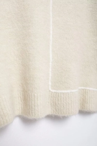 Detailed close-up of beige knitted sweater texture with soft fibers and white contrast stitching