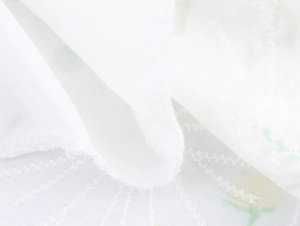Detailed macro view of delicate yellow and green floral embroidery on white fabric edge