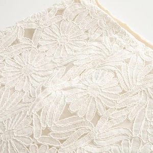 Close-up of intricate white floral embroidery lace on a stylish round neck shirt and skirt