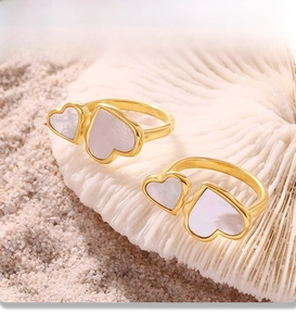 Detail of PVD gold plated double heart rings with natural mother of pearl on white coral