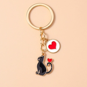Close-up of golden metal keychain featuring black cat and red heart round pendant